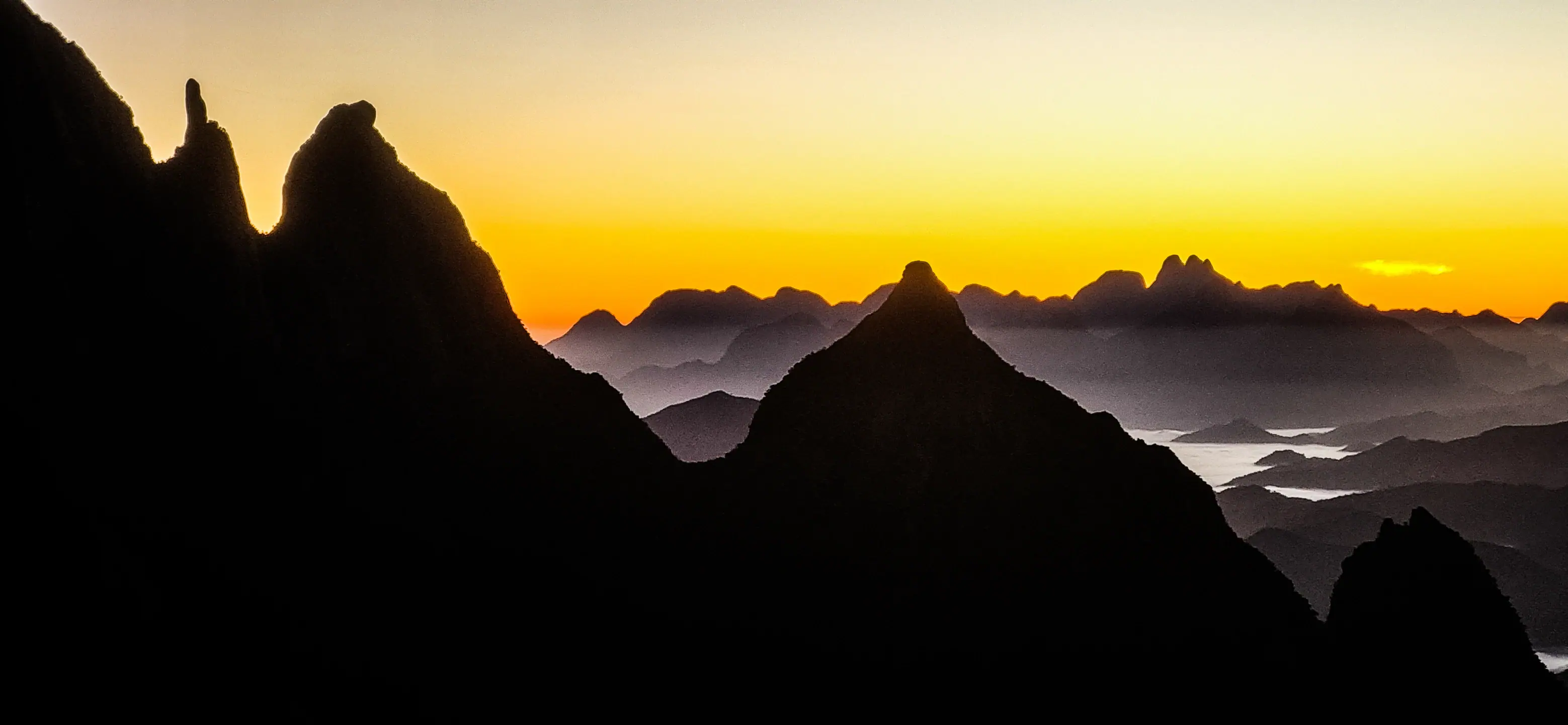 Cumes recortados da Serra dos Órgãos sob luz de amanhecer, com neblina nos vales