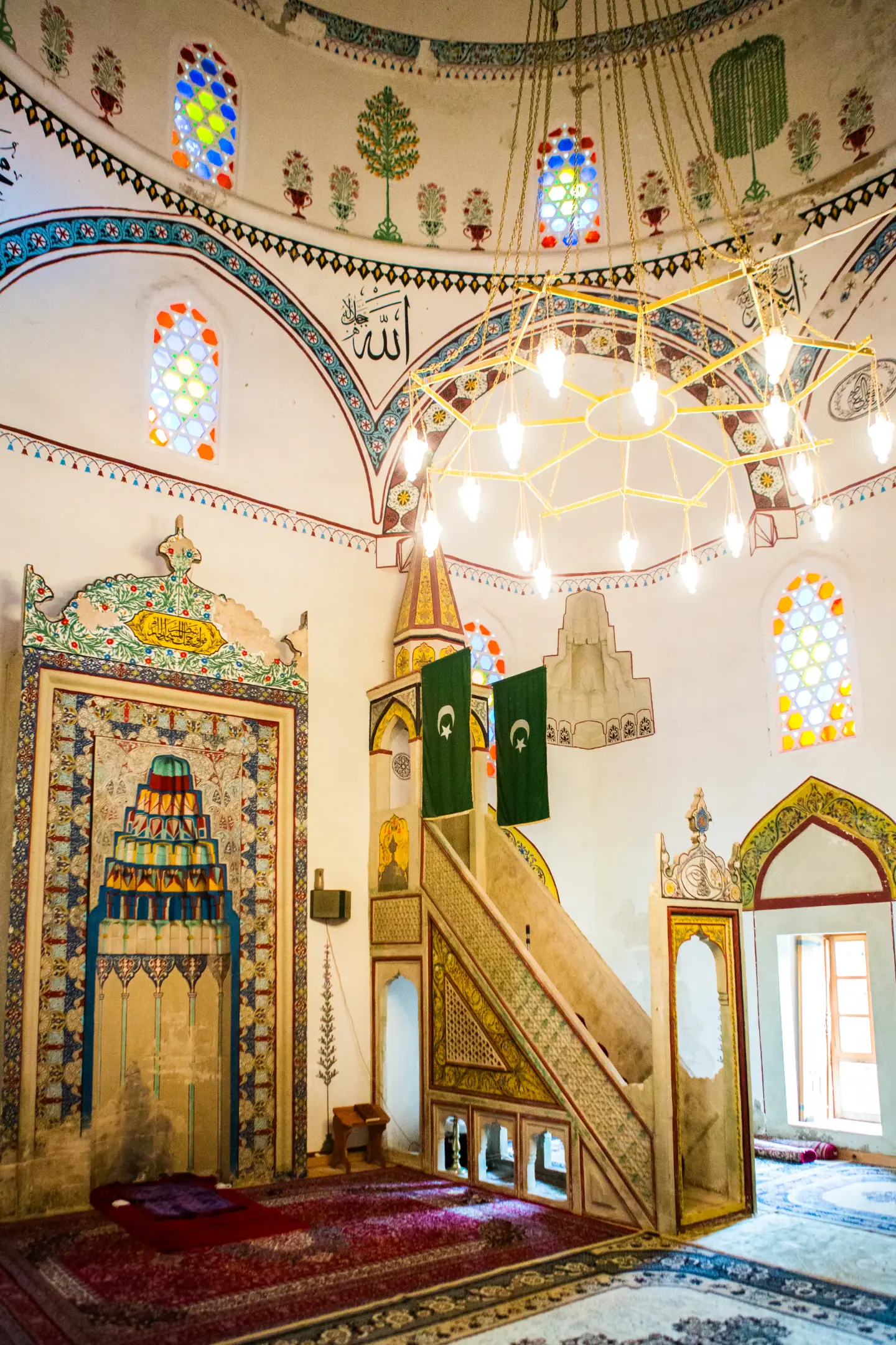 Interior de mesquita em Mostar com mihrab decorado, minbar e vitrais coloridos sob grande lustre