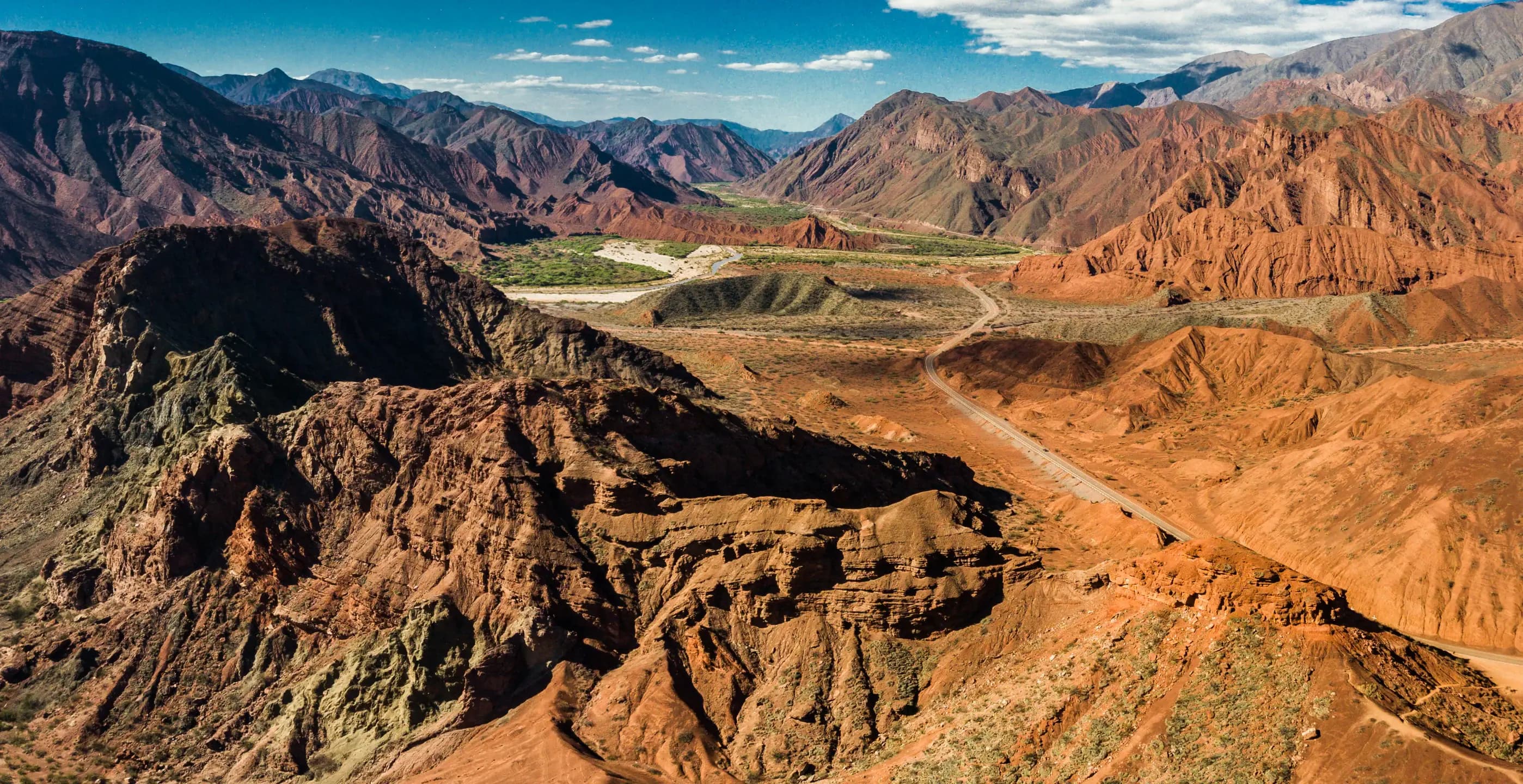 Estrada acompanhando o relevo de um vale entre formações rochosas avermelhadas