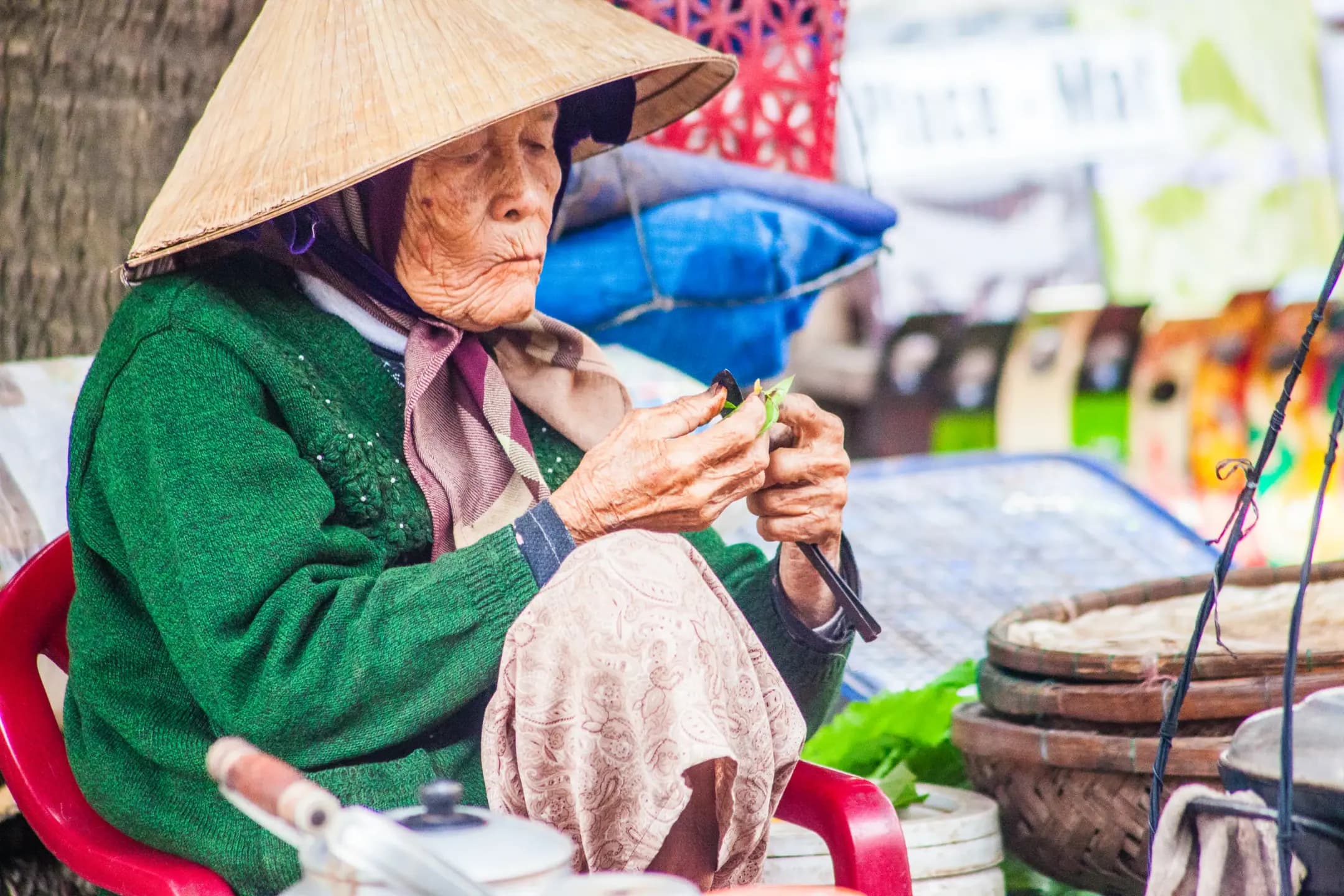 Mulher com chapéu cônico manipulando folhas em banca de rua em Hoi An